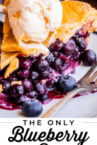 messy slice of blueberry pie on a plate topped with ice cream.