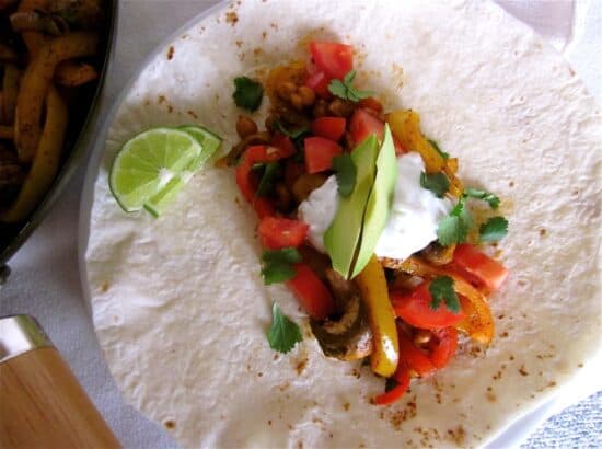 Overhead shot of roasted chickpea fajitas on flour tortilla with lime slices.