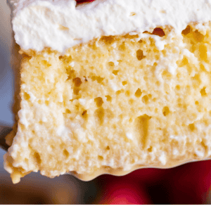 A close-up of a slice of tres leches cake topped with whipped cream and fresh strawberries, with text below that reads Truly the Best Tres Leches Cake, The Food Charlatan. Indulge in this delicious dessert enjoyed by cake lovers everywhere.
