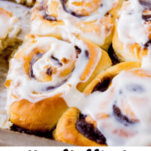A close-up of golden, fluffy cinnamon rolls topped with creamy cream cheese icing, packed closely together in a baking tray. Text at the bottom reads: the fluffiest CINNAMON ROLLS - THE FOOD CHARLATAN.