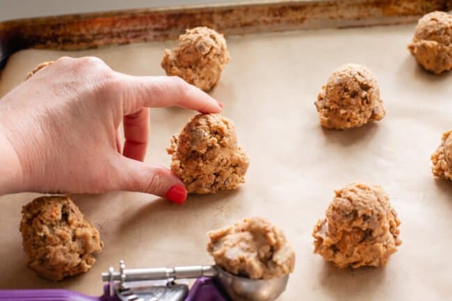 fingers holding a ball of butterfinger cookie dough on a baking sheet, with other cookies lined up.