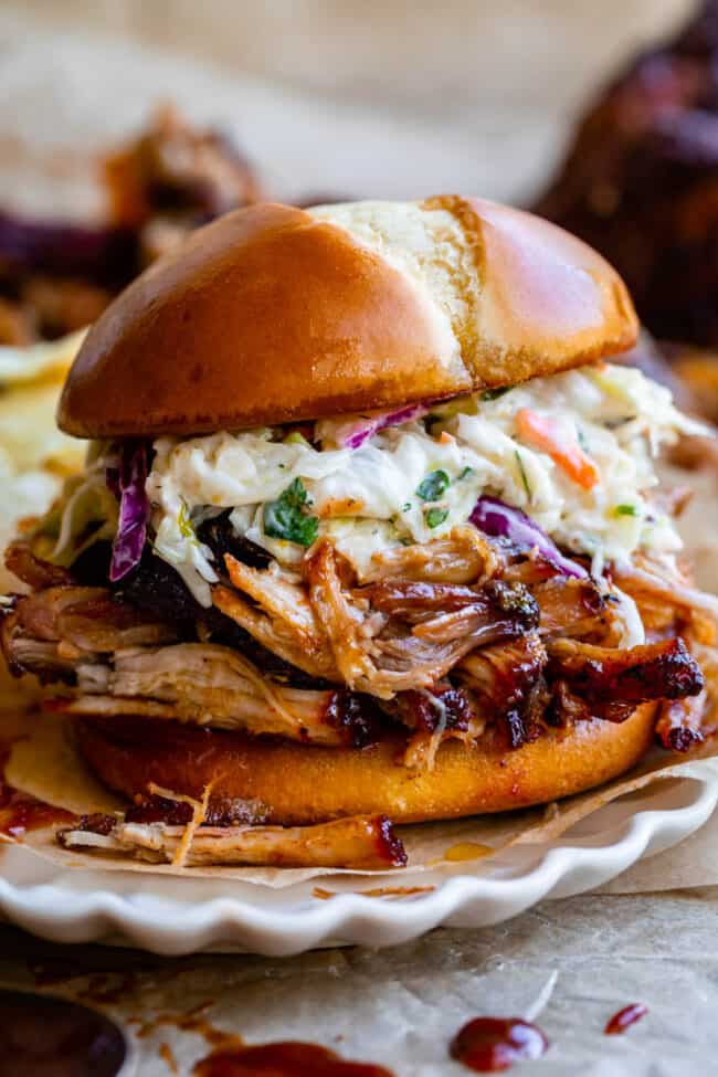 pulled pork sandwich with coleslaw on a white plate.