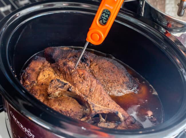 a meat thermometer reading 203 degrees F stuck into cooked pork shoulder in crock pot.
