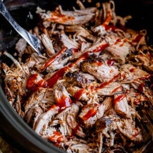 pulled pork in a black slow cooker, topped with barbecue sauce.