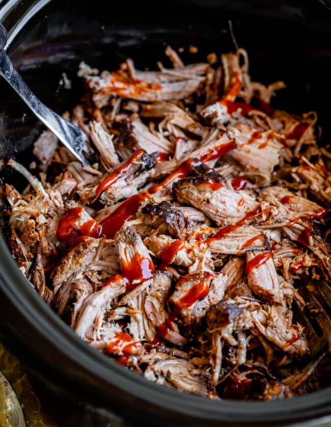 pulled pork in a black slow cooker, topped with barbecue sauce.