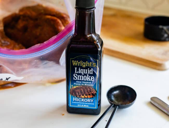 bottle of liquid smoke on white countertop with tablespoon.