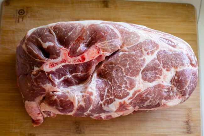 raw pork shoulder on a wooden cutting board, bone in.