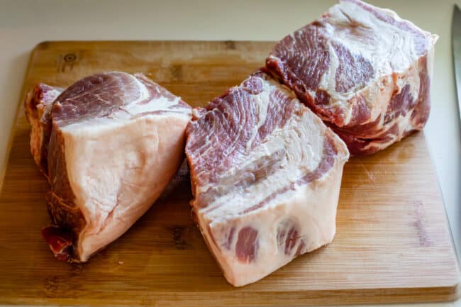 raw pork shoulder on a cutting board, in 3 pieces.