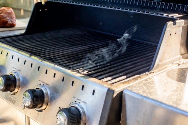 smoke coming up from a smoker box under the grates of a gas grill.