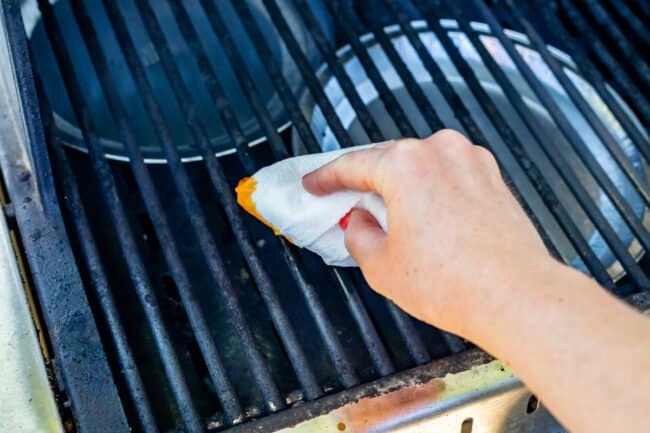 using a crumpled paper towel to oil the grates of a grill.