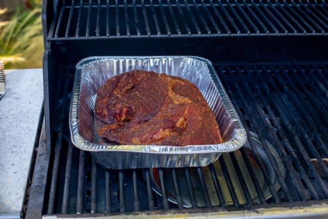 partially cooked pork shoulder in a 9x13 inch disposable pan on a grill.