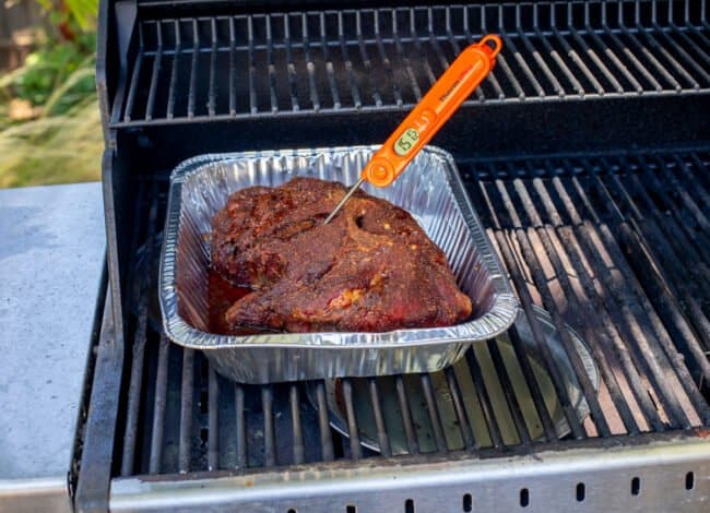 meat thermometer stuck in pork shoulder on a grill, reading 151 degrees Fahrenheit.