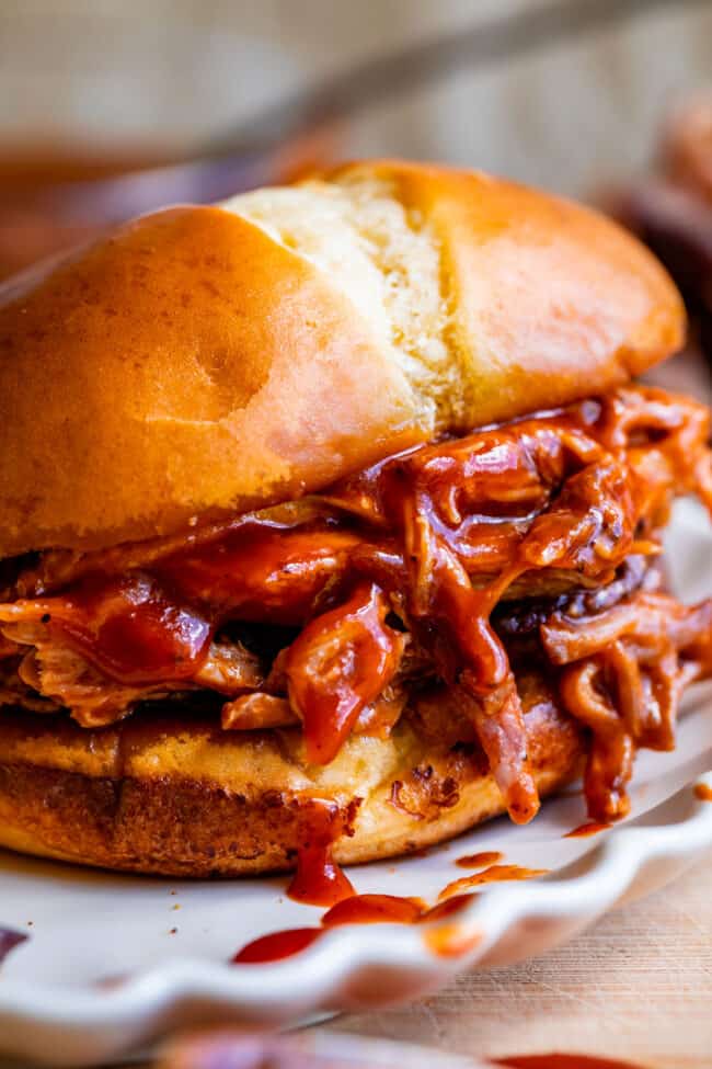 saucy smoked pulled pork on a toasted bun on a plate.
