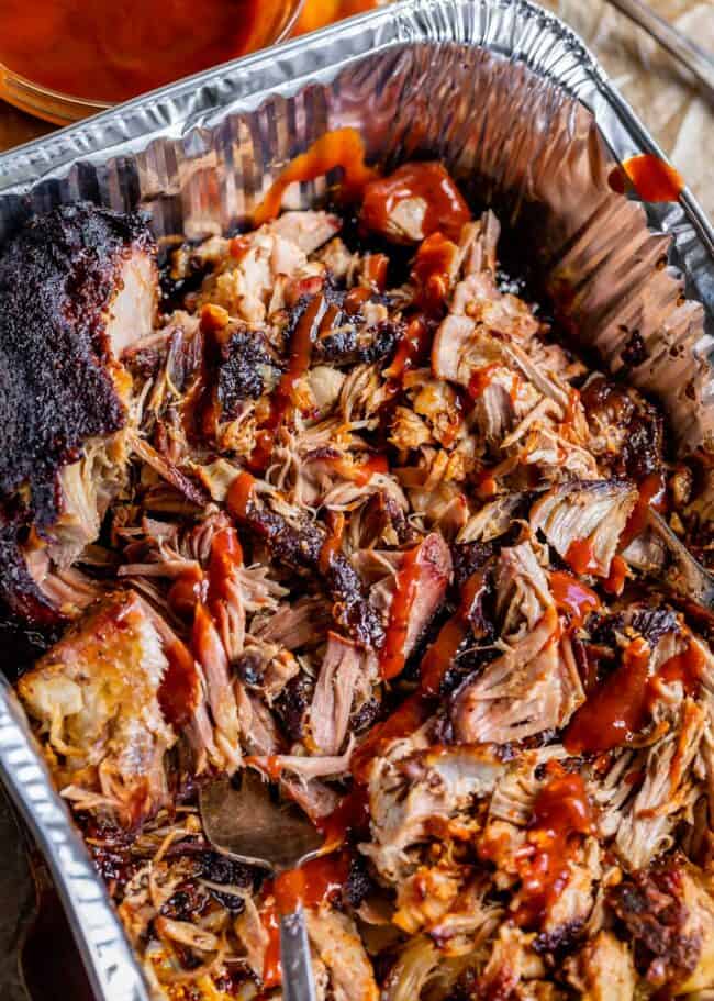 Shredded smoked pulled pork drizzled with bbq sauce in an aluminum pan.