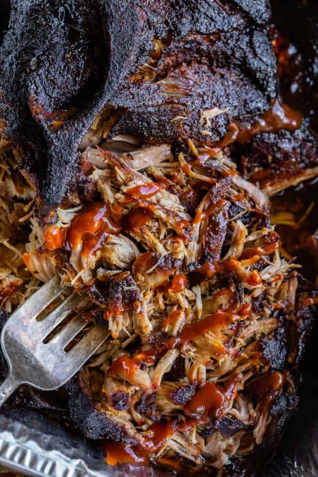 fork sticking into shredded smoked bbq pulled pork topped with bbq sauce.