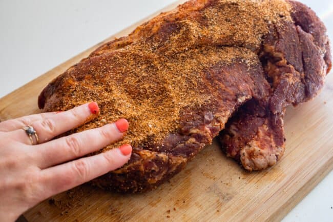 using fingers to rub spice rub into pork shoulder on cutting board.