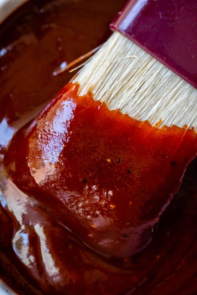 white brush being dipped into bowl of homemade barbecue sauce.