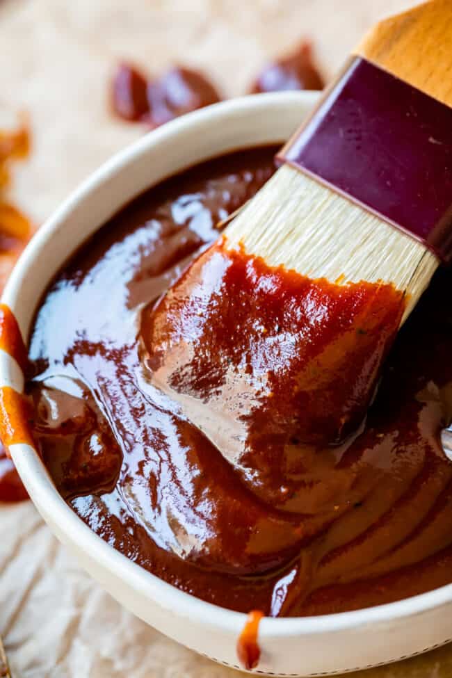 white brush dipping into a white bowl full of barbecue sauce.