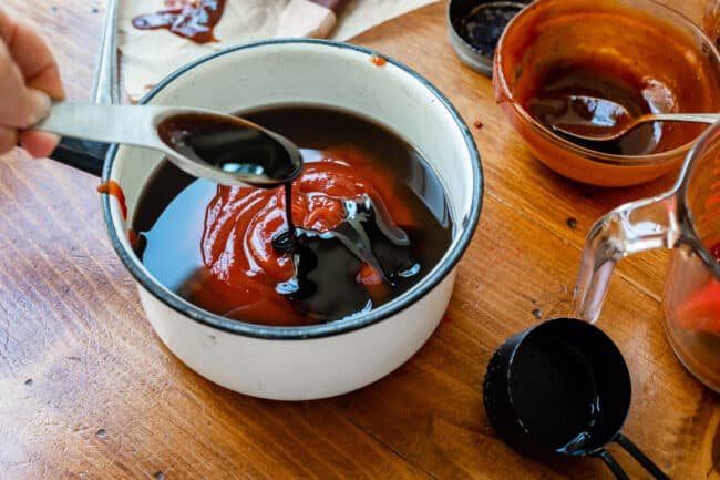 adding molasses to a white pot full of ketchup and other ingredients.