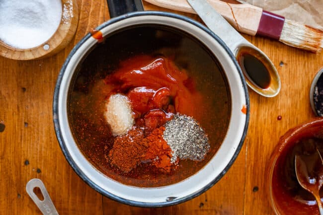 ingredients and spices for barbecue sauce in a white and black pot on a wood table.