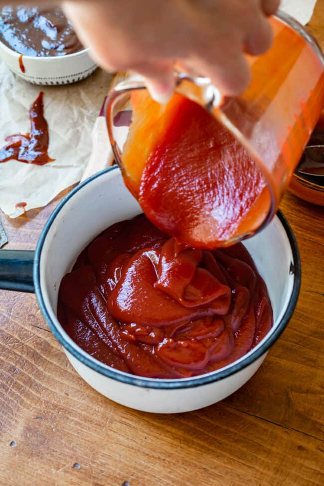 pouring ketchup from a measuring cup into a white saucepan.