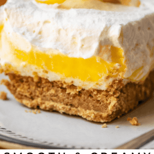 square of lemon lasagna with whipped cream and cream cheese and lemon on plate.