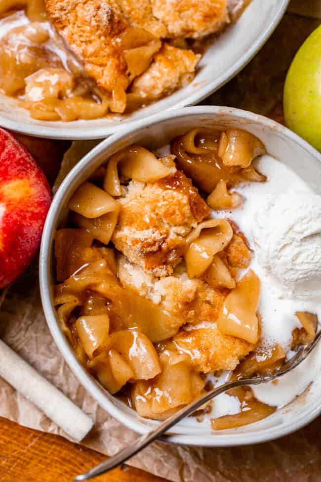 best apple cobbler recipe in a white bowl with ice cream and red apple on the side.