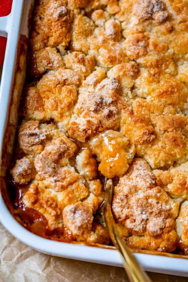 apple cobbler with biscuit cake topping with gold spoon in a white dish.