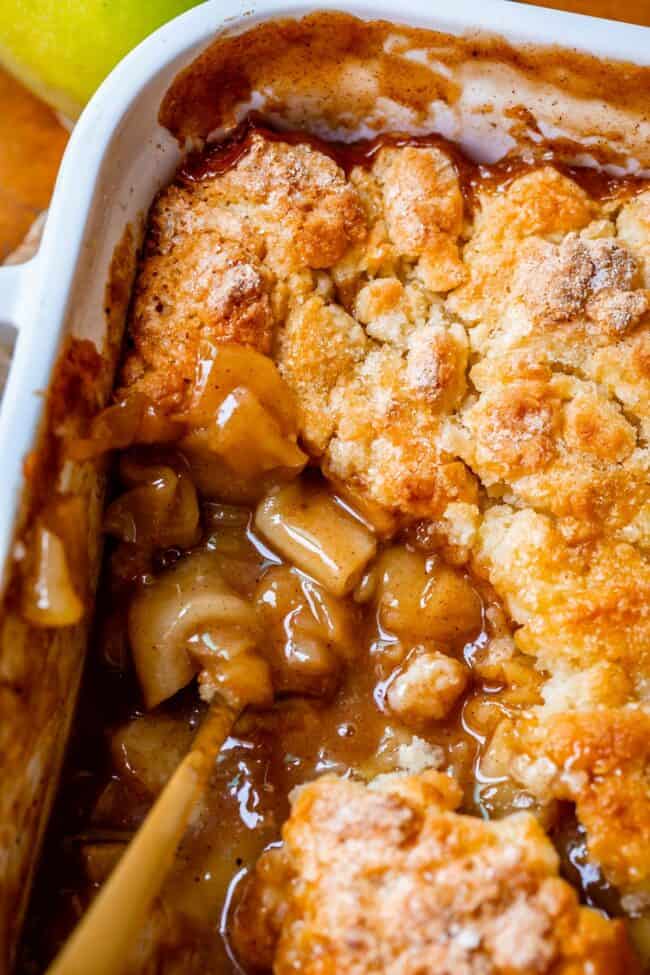 the best apple cobbler recipe in a white pan with gold spoon in apples.