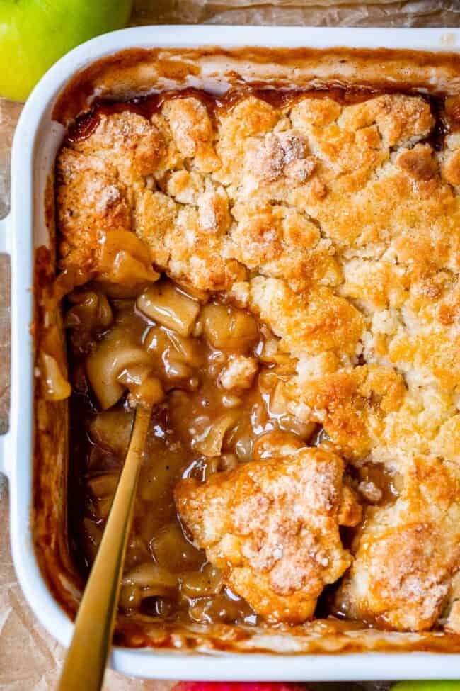 overhead shot of apple cobbler in a white casserole dish with gold spoon.