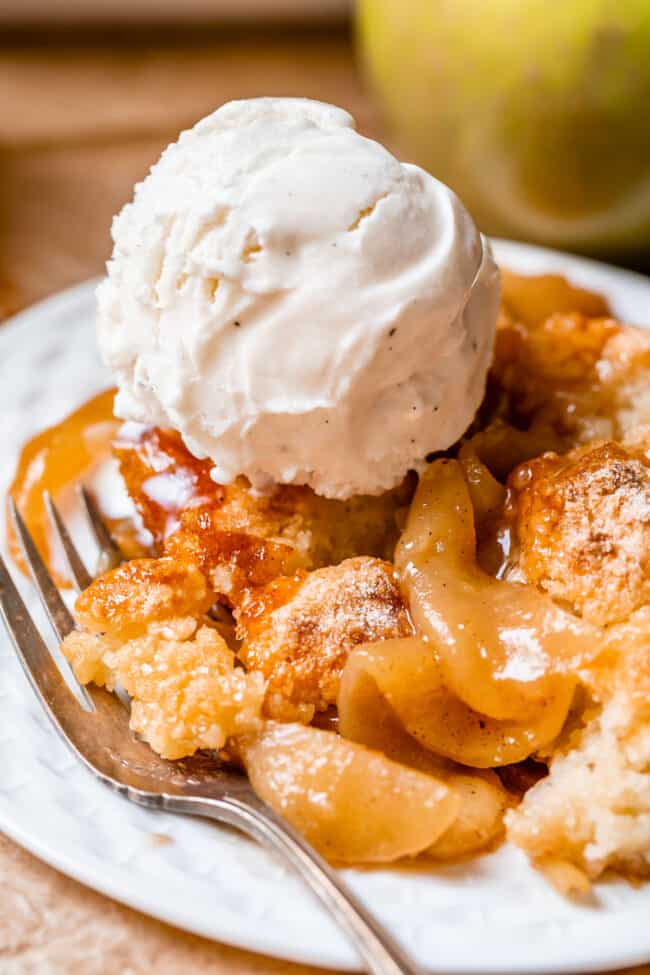 easy apple cobbler on a white plate with fork and topped with vanilla ice cream.