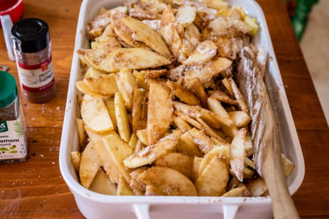 raw apples covered in flour and sugar in a white casserole dish.