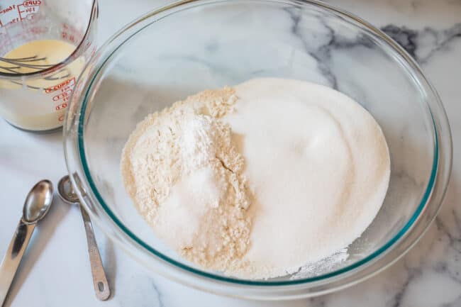 flour and sugar and salt and baking powder in a clear glass bowl with teaspoons on side.
