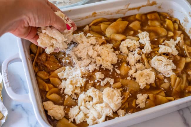 adding a floury biscuit topping to an apple cobbler in a white casserole dish.