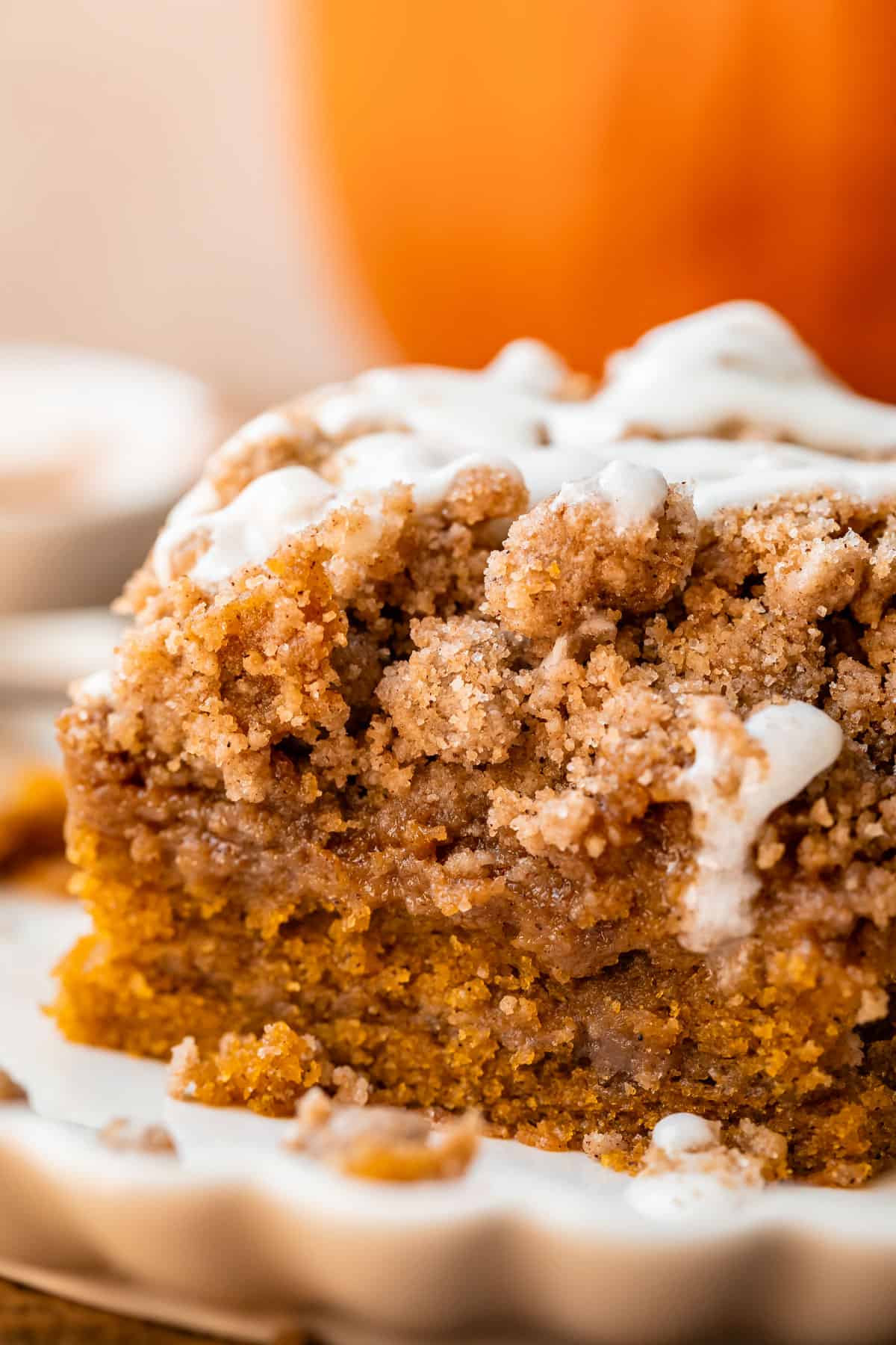 pumpkin streusel coffee cake on a white scalloped plate with pumpkin in the background.