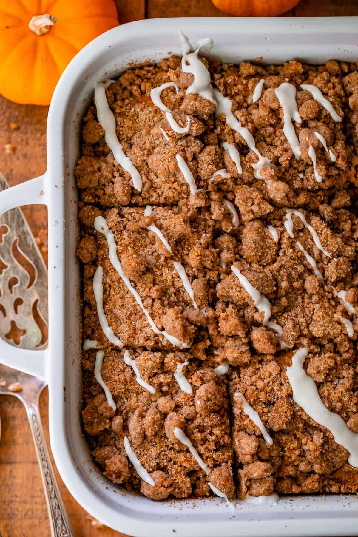 pumpkin streusel coffee cake in a white pan with glaze drizzled on top, shot from overhead.