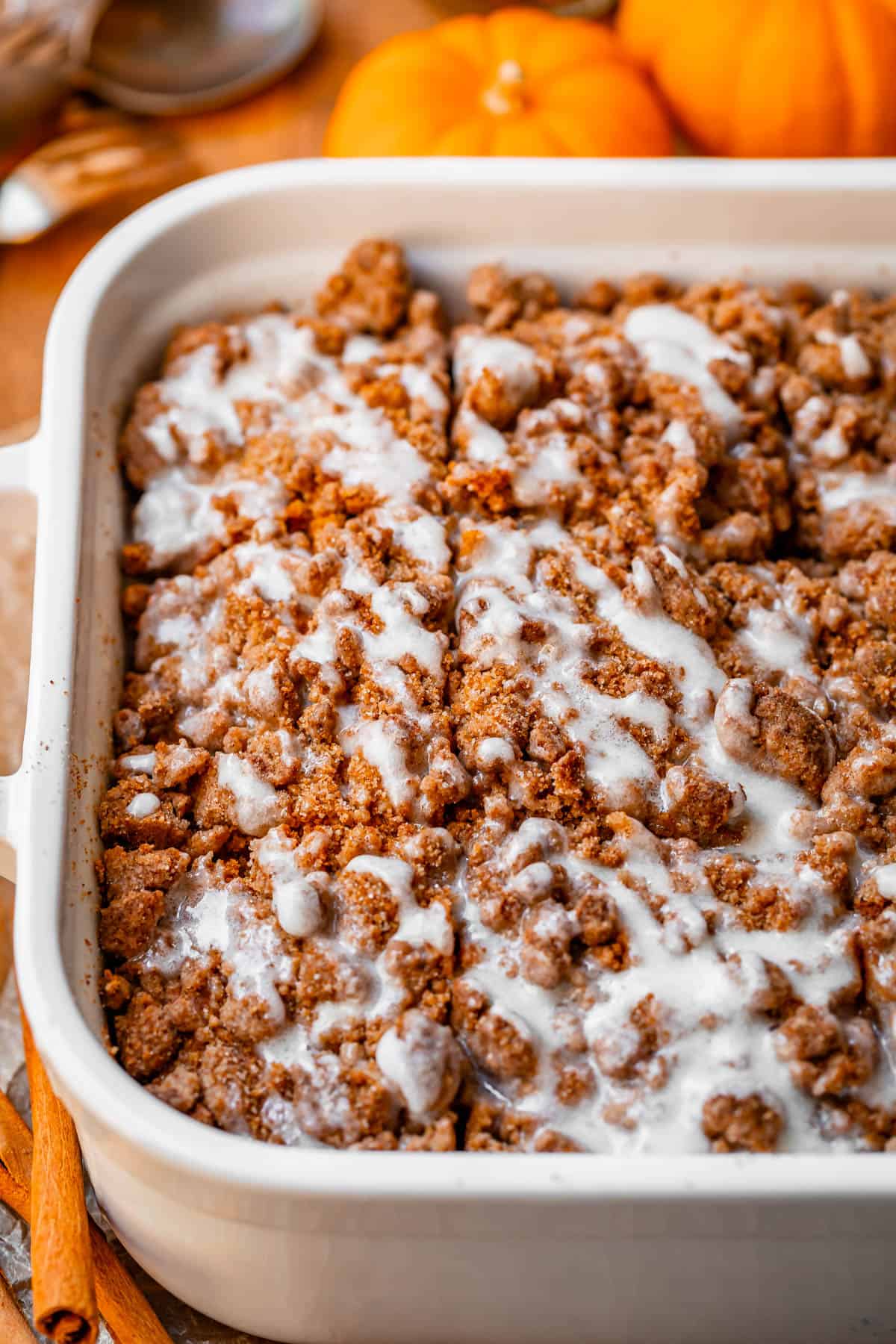 pumpkin streusel coffee cake in a white dish with glaze drizzled on top.