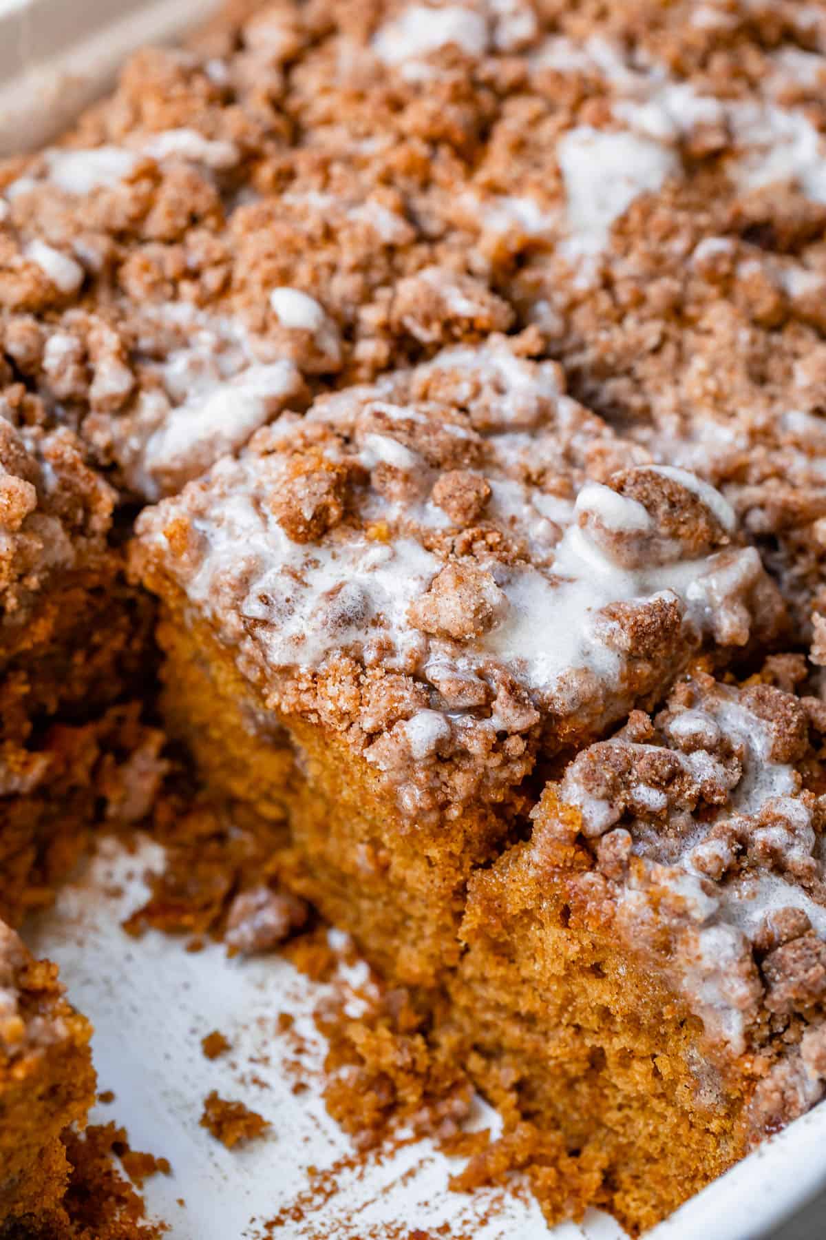 pumpkin coffee cake with glaze in a white pan.