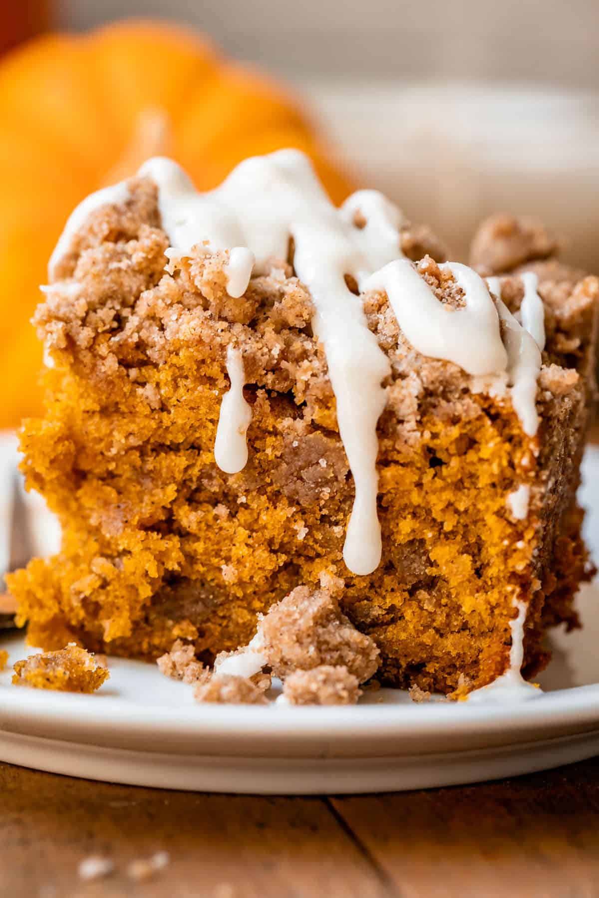 pumpkin spice coffee cake on a white plate with pumpkins in the background.