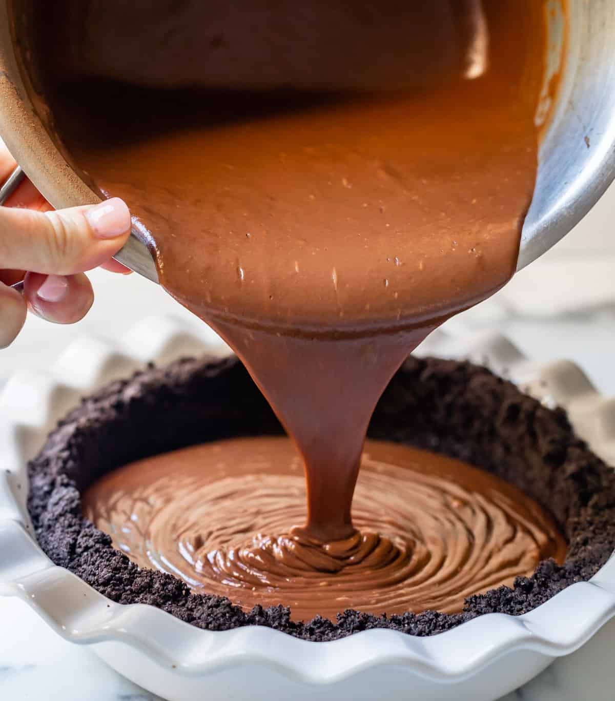 pouring chocolate pudding into an oreo pie crust.