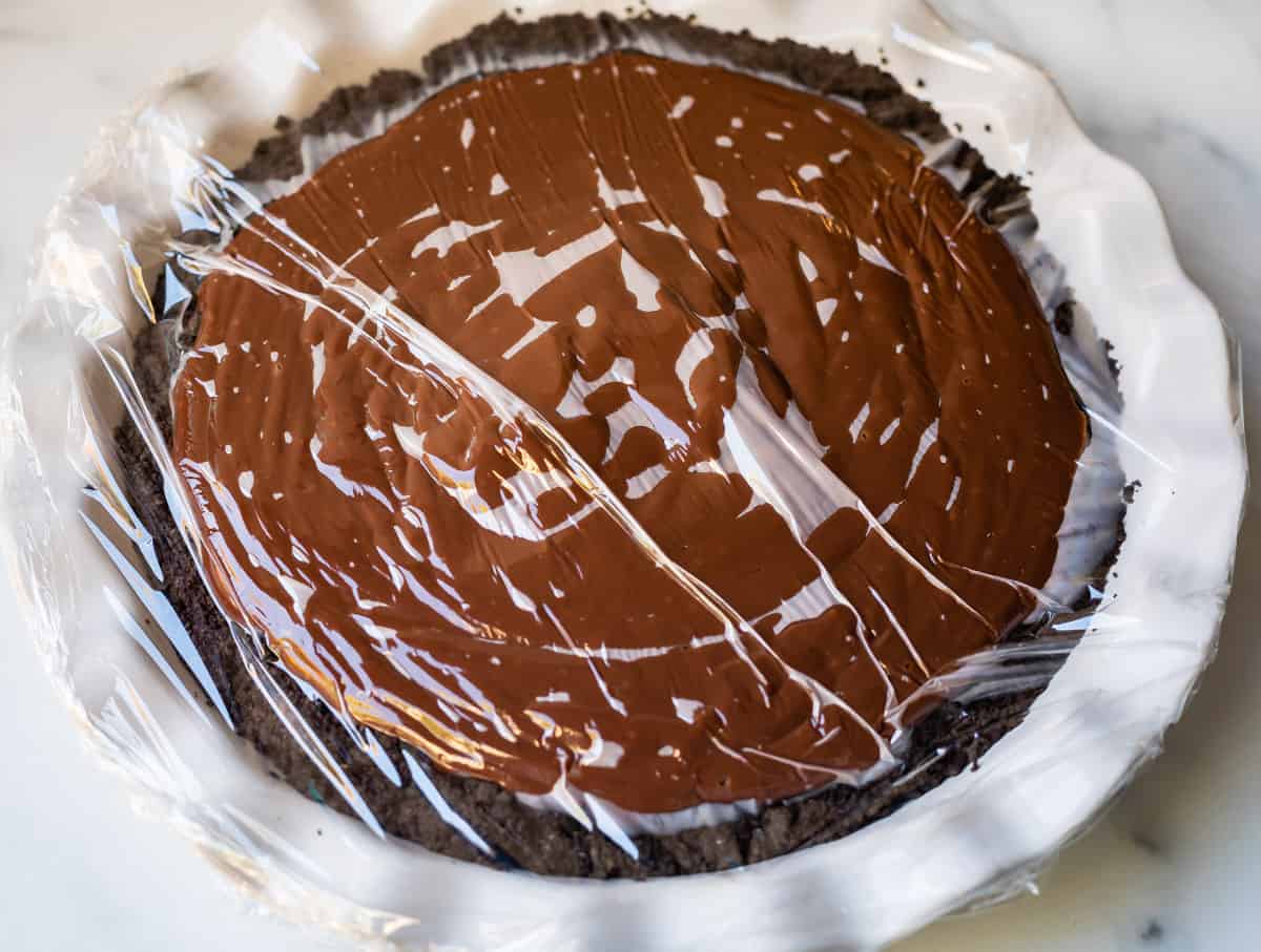 chocolate cream pie covered in plastic wrap in white dish.