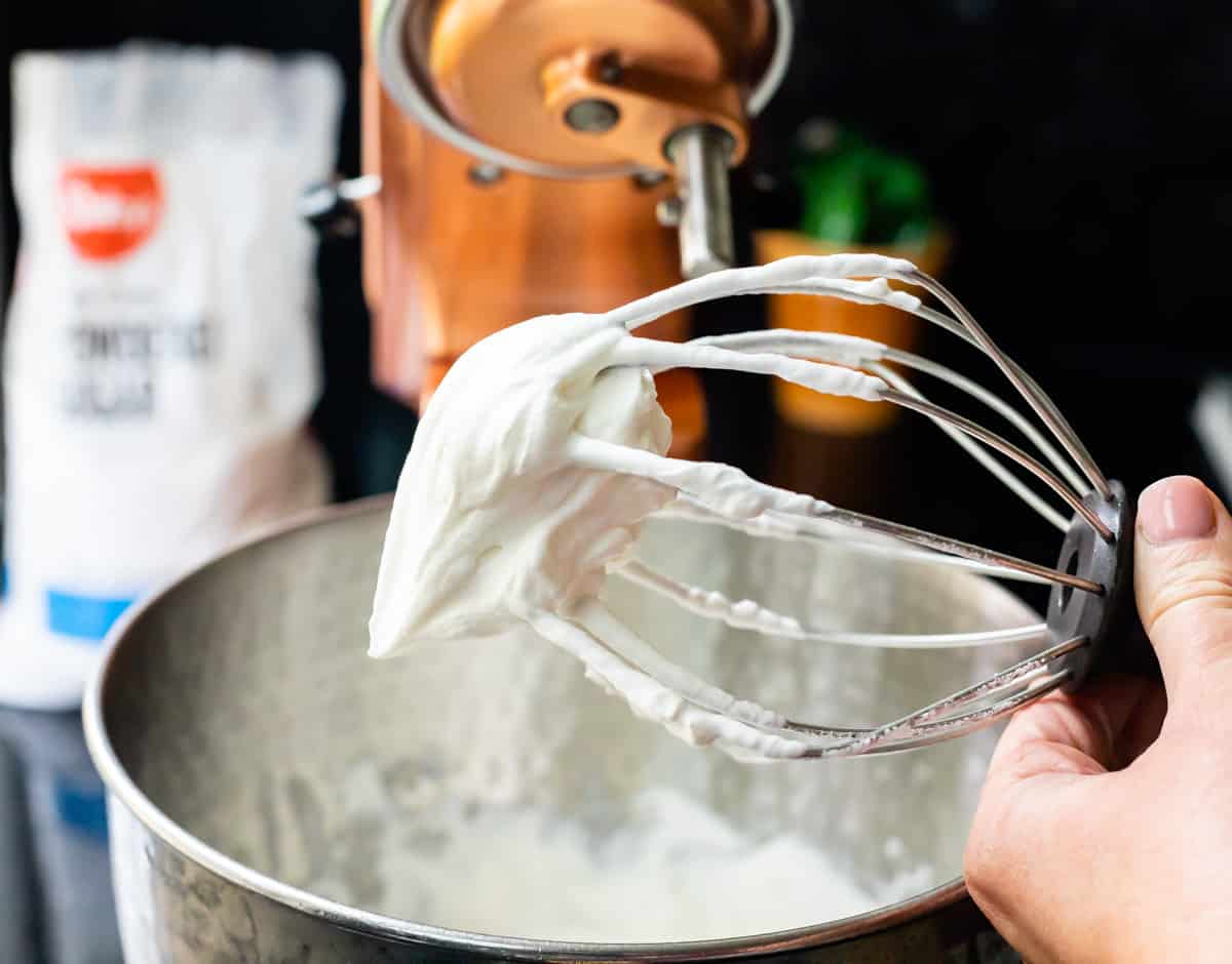 whipped cream stiff on a beater with kitchenaid in background.