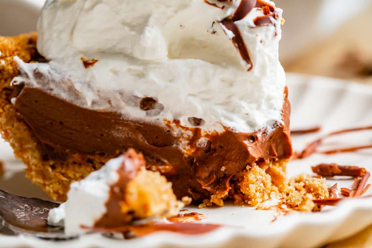 messy chocolate cream pie on a plate with graham crust and whipped cream.