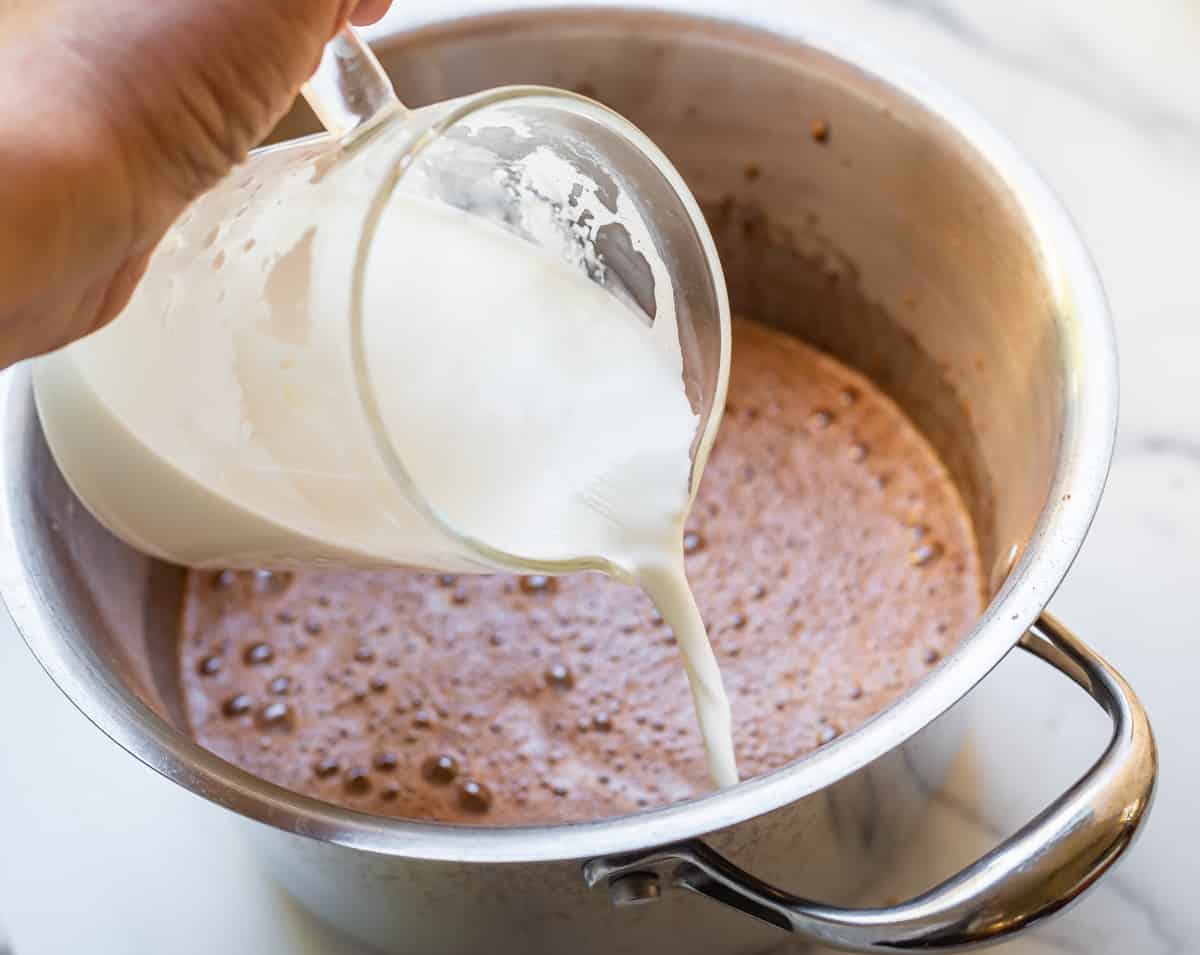 adding hot milk to a pot of eggs and milk.