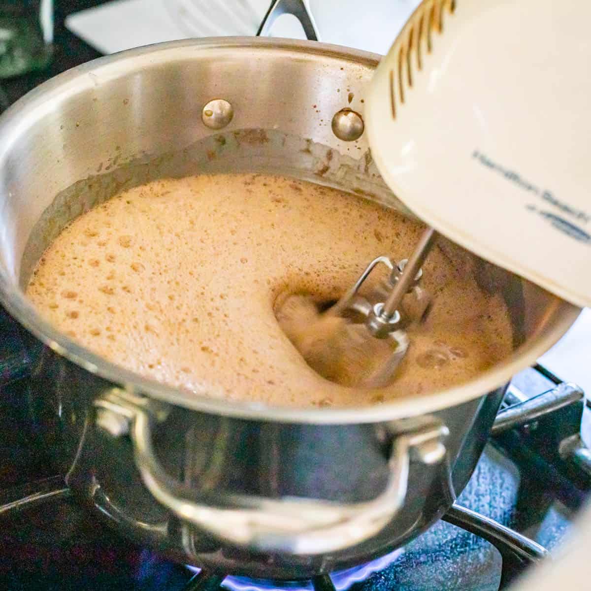 beating pudding mixture with a hand mixer on the stove with heat on.