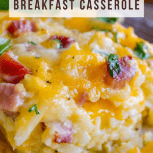 Close-up of a cheesy hashbrown breakfast casserole with melted cheese, savory ham chunks, and fresh parsley. Text overlay reads Cheesy Hashbrown Breakfast Casserole and The Food Charlatan.