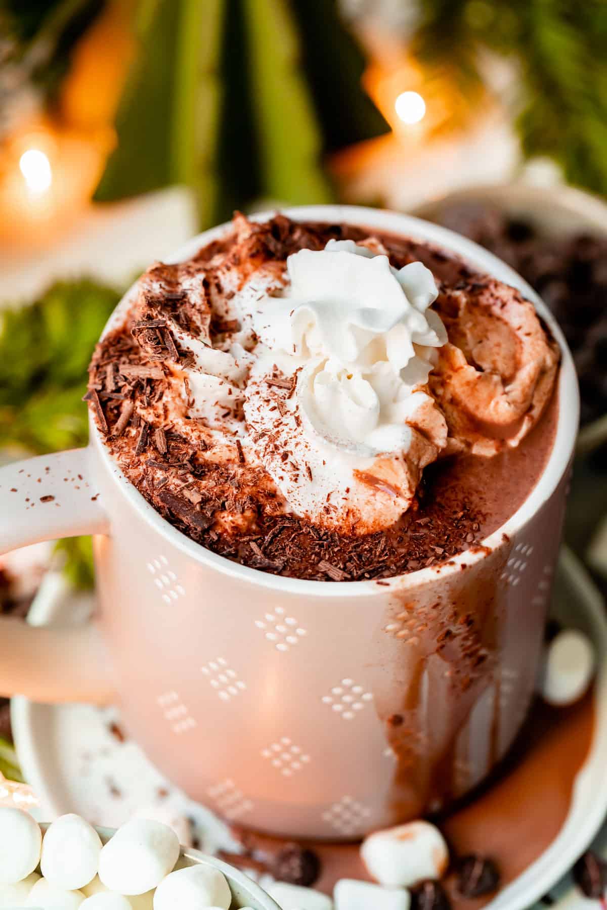 a gray mug of homemade hot chocolate on a table with whipped cream and greenery in the background.
