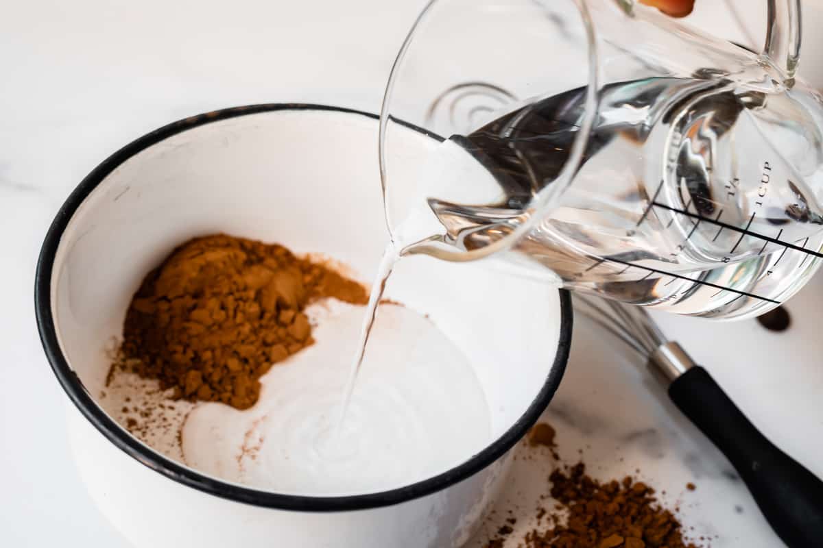 pouring water from a glass measuring cup into a white pot with cocoa powder.