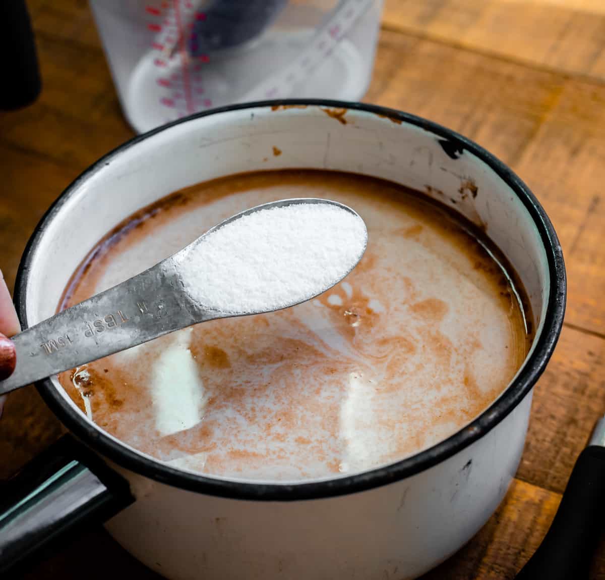 Adding sugar to a white pot full of hot chocolate.