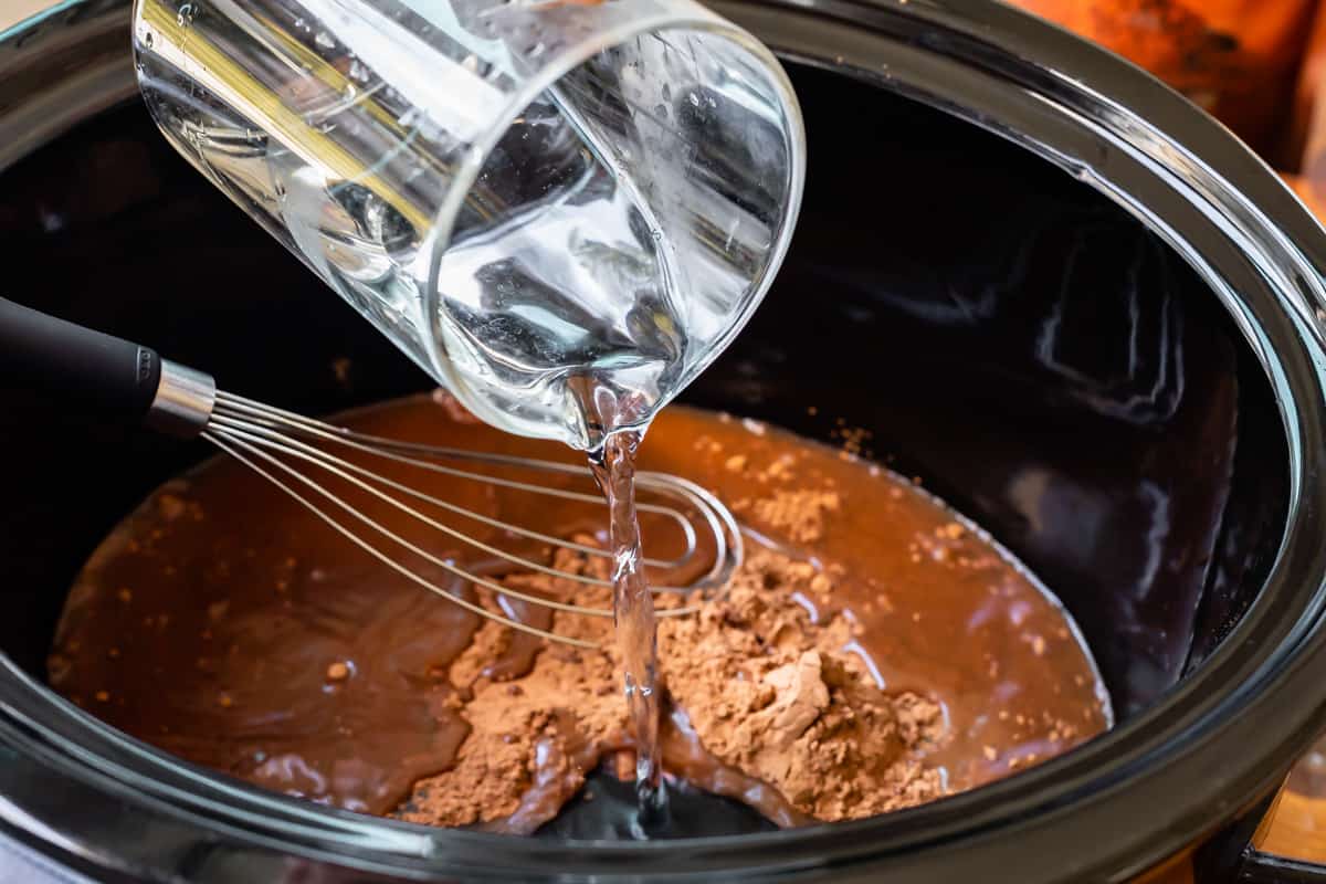 Adding water to a black crock pot with cocoa powder.